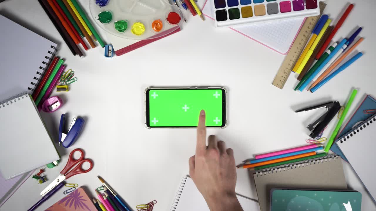 Man is swiping left then tapping on the smartphone with green screen lying among stationery