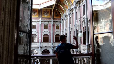 tourist waves to courtyard of nations from balcony of palacio da bolsa, porto