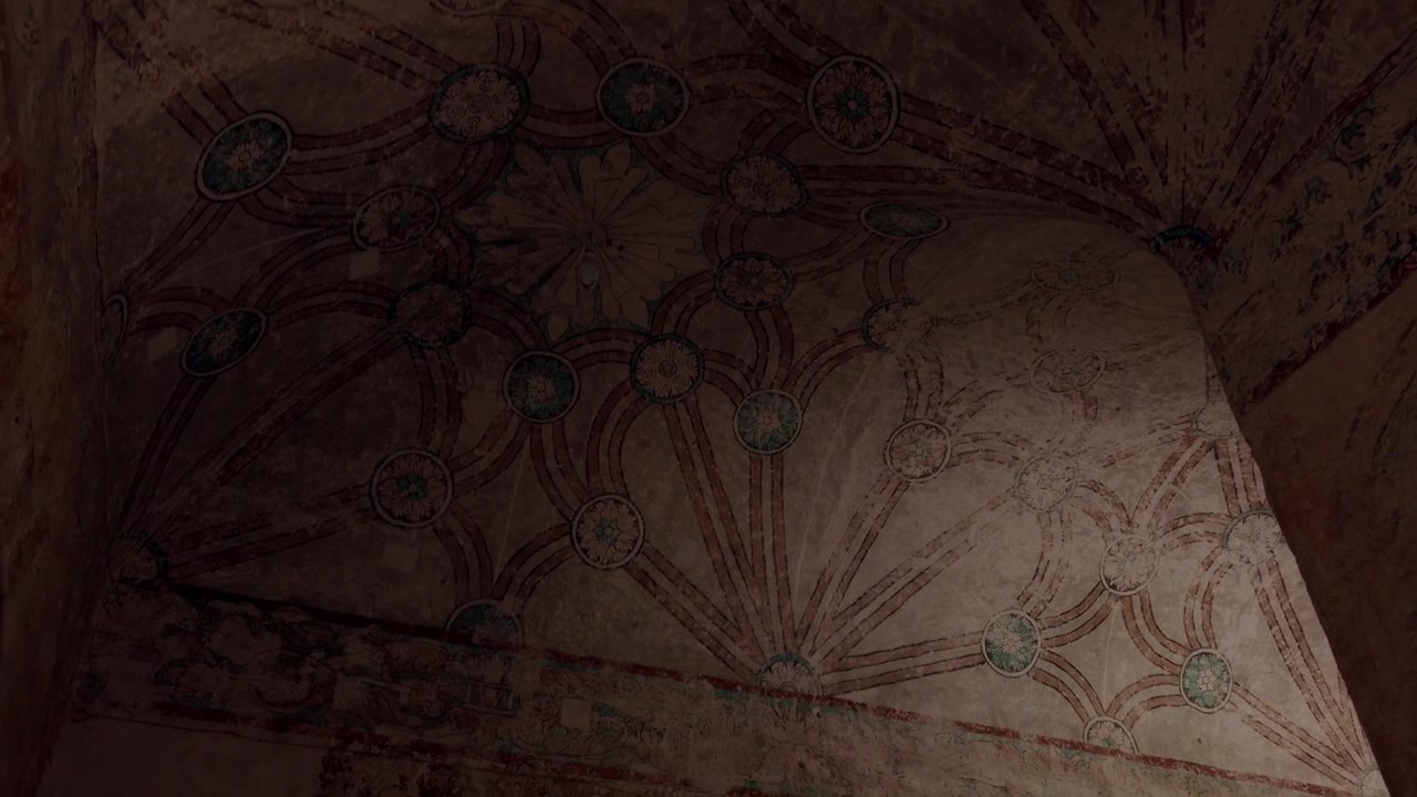 Vista verso l'alto di un soffitto storico dipinto con motivi floreali decorativi e dettagli artistici invecchiati all'interno di un antico interno architettonico