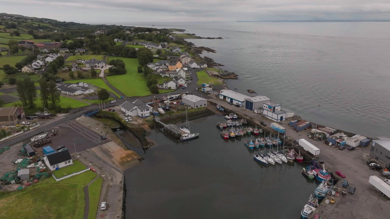 Un'autentica prospettiva aerea del molo di Greencastle con barche da pesca, architettura locale e la costa frastagliata della Contea di Donegal, Irlanda