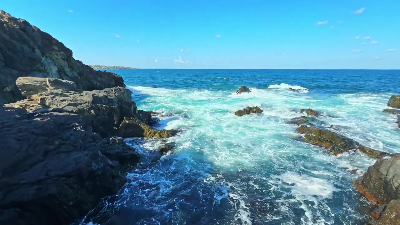 Wellen schlagen an Felsen am Meer unter klarem blauem Himmel in einem Küstengebiet bei Tageslicht