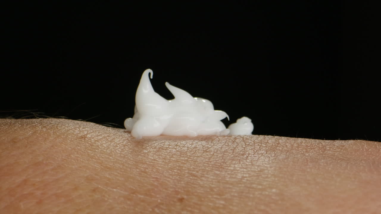 Young man squeezing a white moisturizer from a tube on his hand close-up. Morning routine. Beauty and care concept. Skin texture.