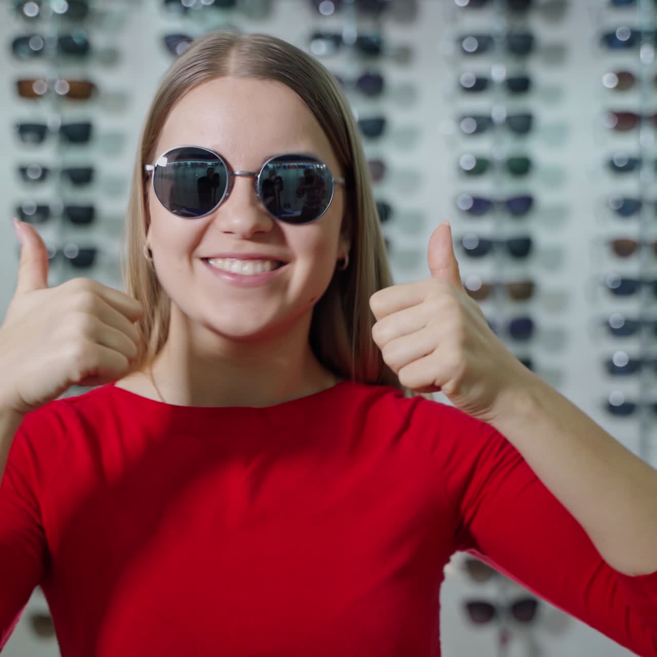 Pretty girl in fashionable sunglasses in the store. Portrait of a lovely girl showing Ok sign by hands on the background of sunglasses at optics.