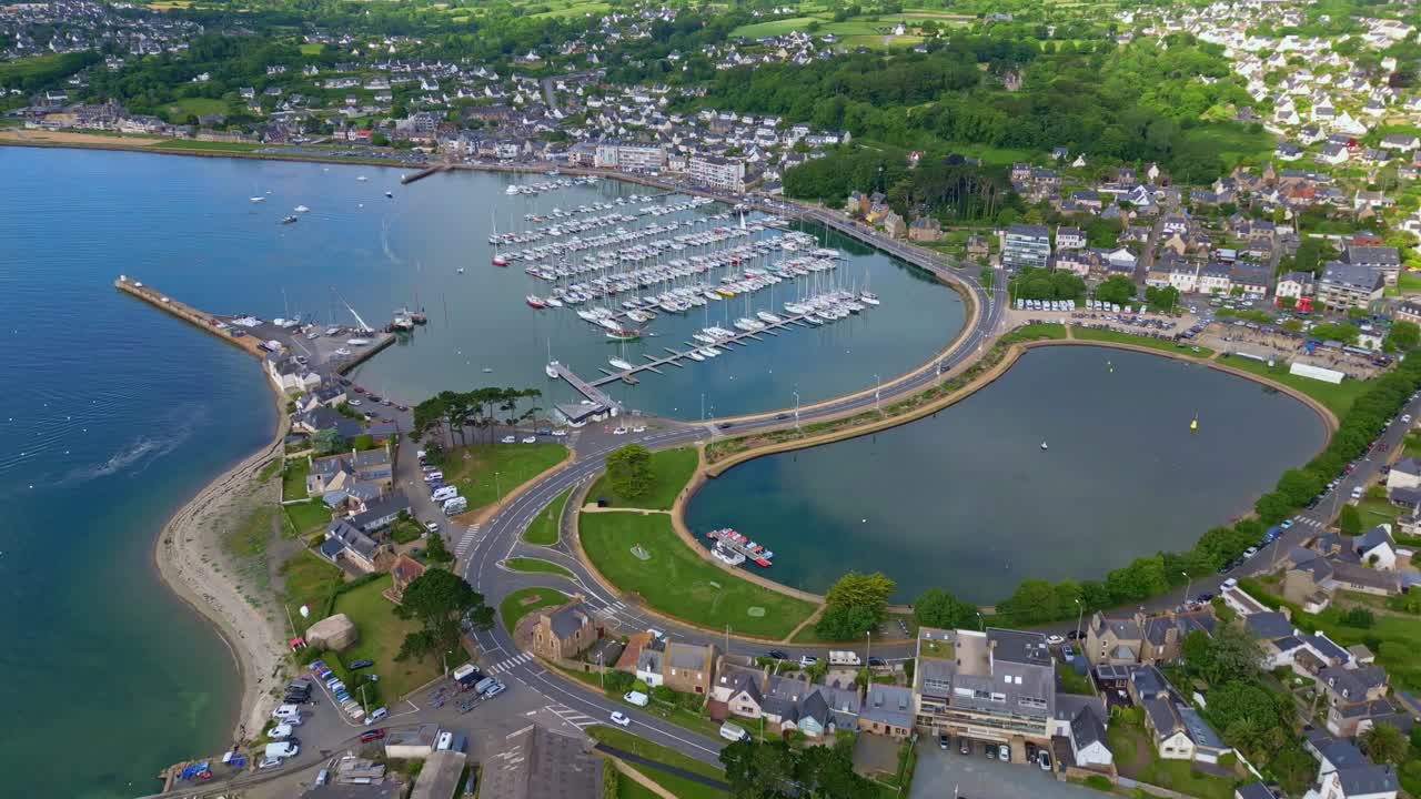 Perros-Guirec harbor with sailboats, coastal town, causeway, and green countryside, Brittany, France. Aerial drone forward