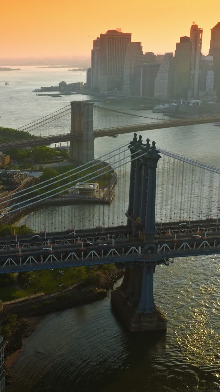 Manhattan and Brooklyn Bridges over East River. Silhouettes of New York skyscrapers at the backdrop of orange skies. Vertical video