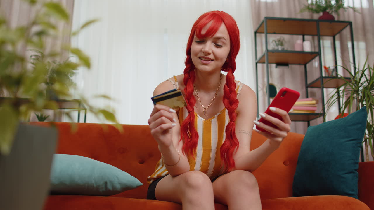 Donna seduta sul divano usando carta di credito e smartphone mentre trasferisce denaro per lo shopping online