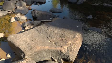 drone flying low altitude over large stones peaking out of shallow river water