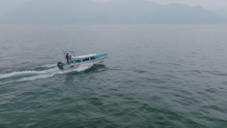 tracked aerial footage following and passing a passenger speedboat that is going across the water of lake atitlan in guatemala in the haze