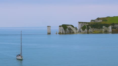 sailing boat gently floating by on calm english channel near old harry rocks white chalk cliff formation in early morning with blue sea ocean water near poole, dorset uk 4k