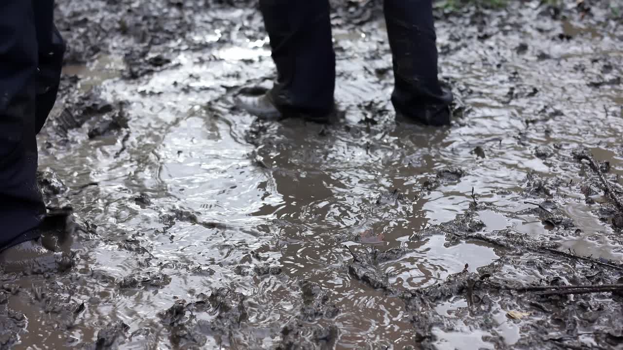Two young children playing in a muddy puddle, wearing waterproof clothing