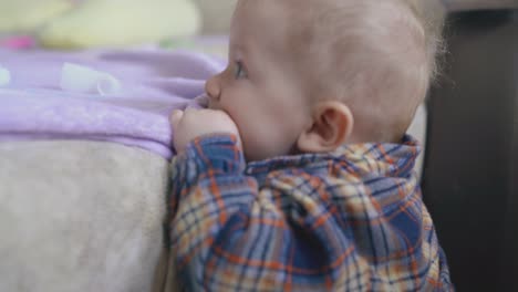 little boy in shirt climbs on large bed chewing pink plaid