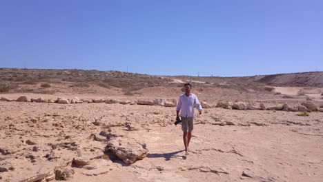 Aerial-shot-of-a-photographer-approaching-the-edge-of-the-cliff-and-taking-pictures-of-the-beautiful-sea-caves-below-him