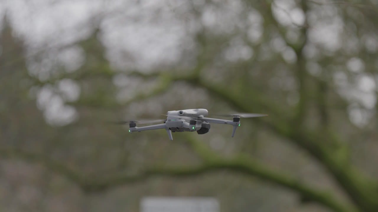Close up of drone hovering in flight with trees blurred in background