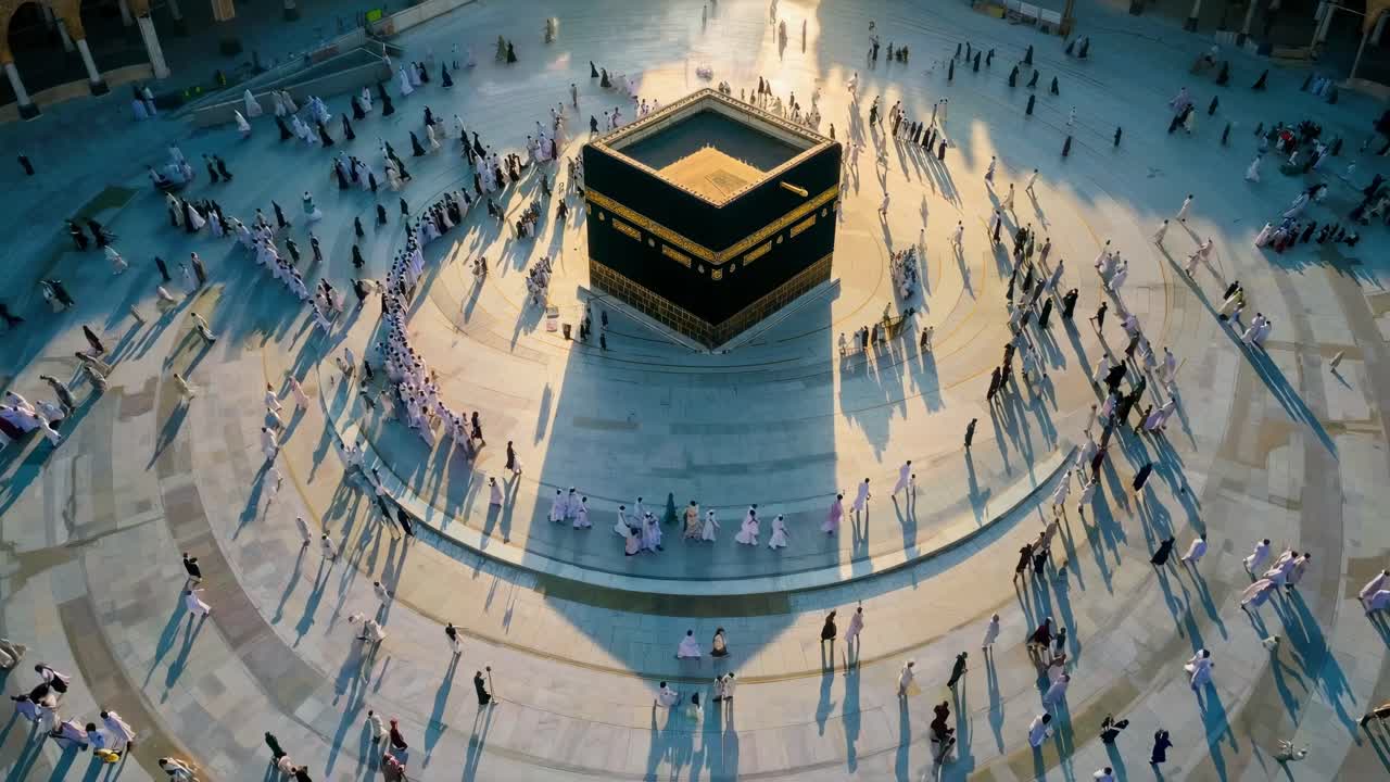 Aerial video view of people circling a central structure, casting long shadows on a sunlit plaza