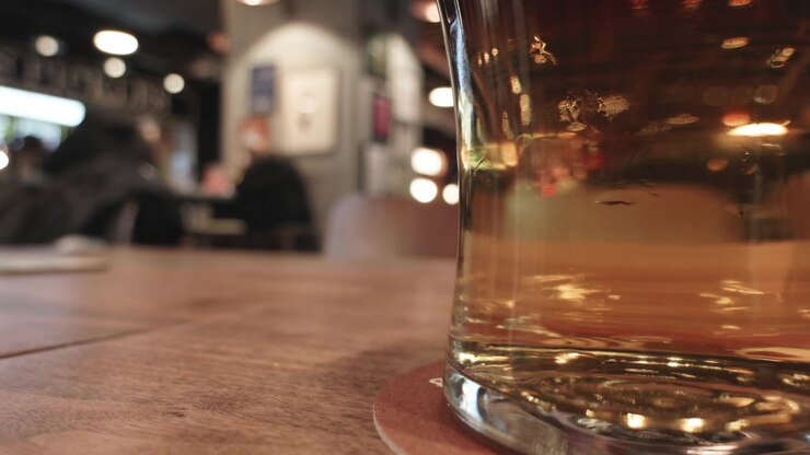 Primo piano di un bicchiere di birra poggiato su un tavolo di legno in un caffè vivace. Ideale per contenuti di ospitalità o lifestyle.