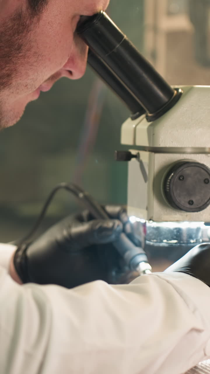 A close-up view of a focused technician in a lab coat carefully working on an electronic circuit board under a microscope