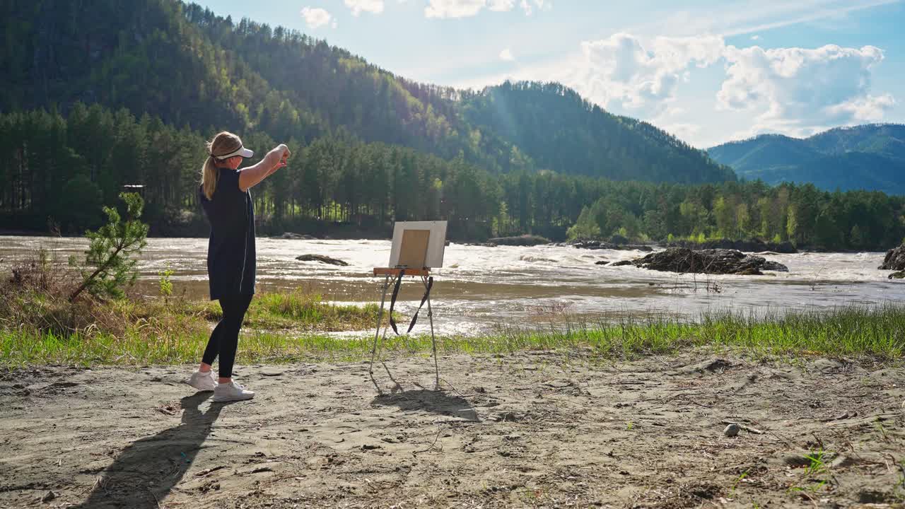 Woman painting a landscape by a river in the mountains