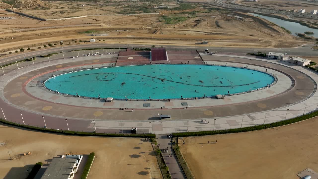 Ripresa aerea con drone in movimento all'indietro sopra una fontana d'acqua ovale appena installata accanto a un'autostrada nella città di Bahria a Karachi, Pakistan, in una giornata di sole