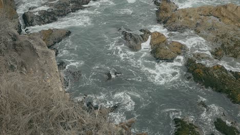 looking over coastal sea cliffs at water crashing into cliffside and rocks on overcast summer day