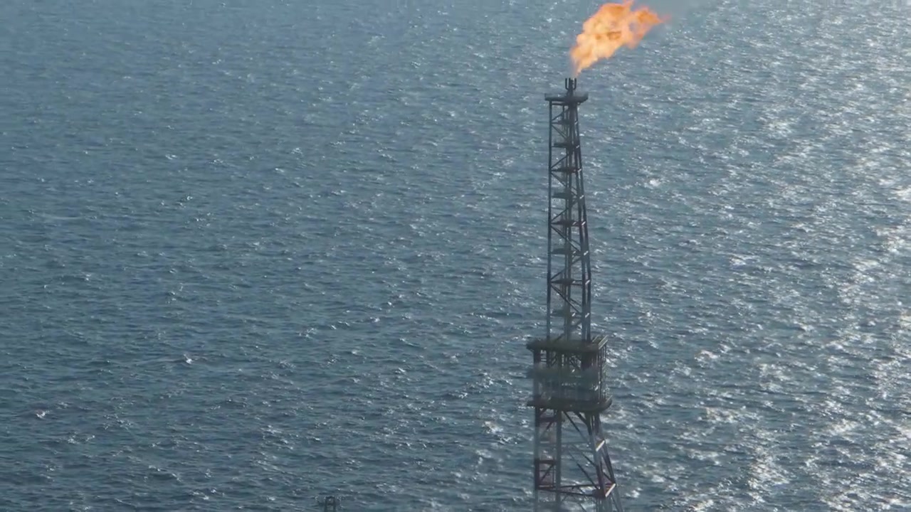 Imágenes aéreas cinematográficas en primer plano enfocadas en la antorcha de gas en llamas de una plataforma petrolera industrial en alta mar con el telón de fondo de aguas profundas y abiertas del mar.