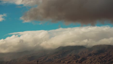 the wind pushes snow and rainstorm clouds roll up against the mountains in the mojave desert as a storm approaches - time lapse