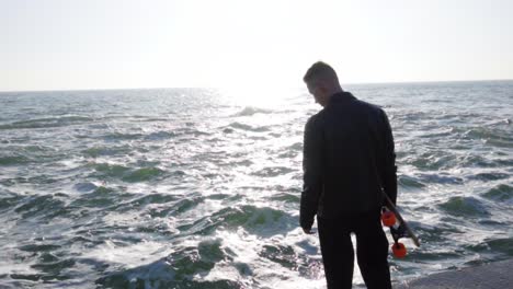 Young-man-holds-his-longboard-standing-by-the-sea