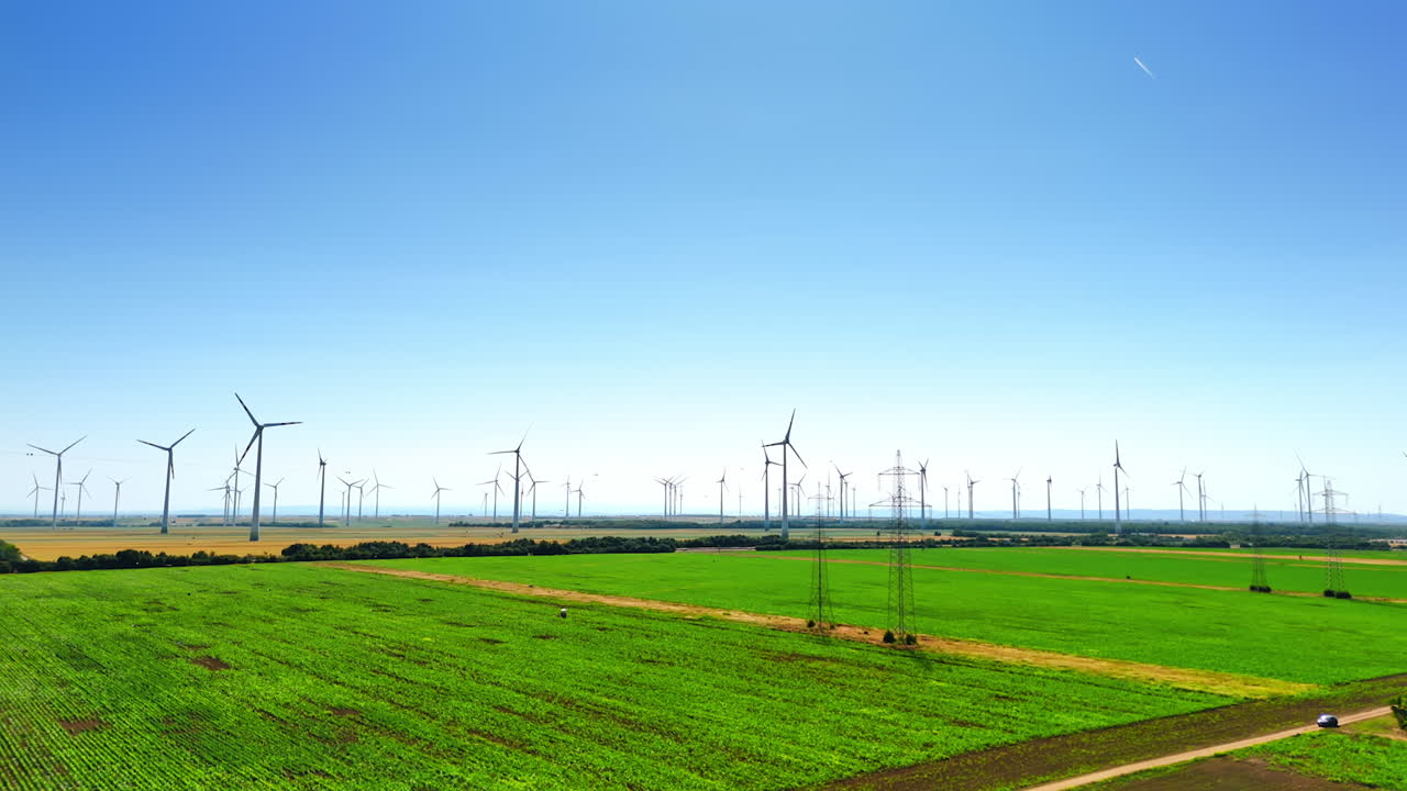 Footage above the green farmlands on sunny day. Modern wind farms produce green energy in the fields