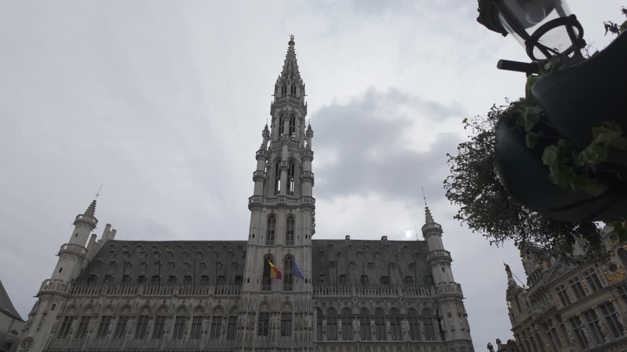 Tall spire of Brussels Town Hall rising above Grand Place, framed by cloudy skies, Belgium