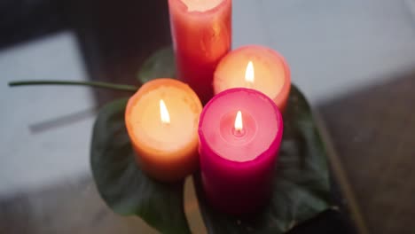 Velas-De-Durazno-Y-Rosa-Encendidas,-Encima-De-Una-Hoja-De-Monstera,-En-Un-Panel-De-Vidrio