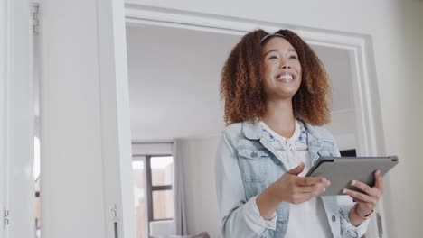 Happy-biracial-woman-using-tablet-standing-at-home,-smiling-in-slow-motion