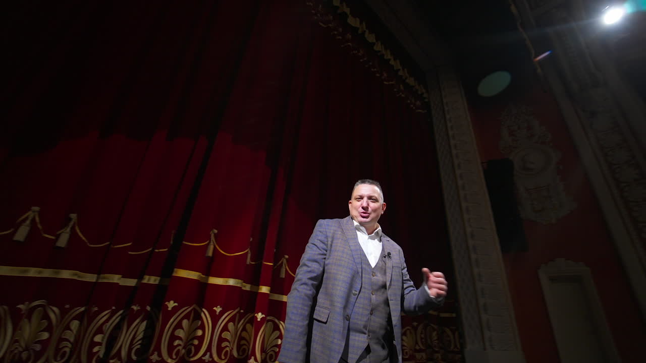 Comedian rehearsing on scene. Happy male actor performing in the theater dancing and singing on stage. Orbital shot.