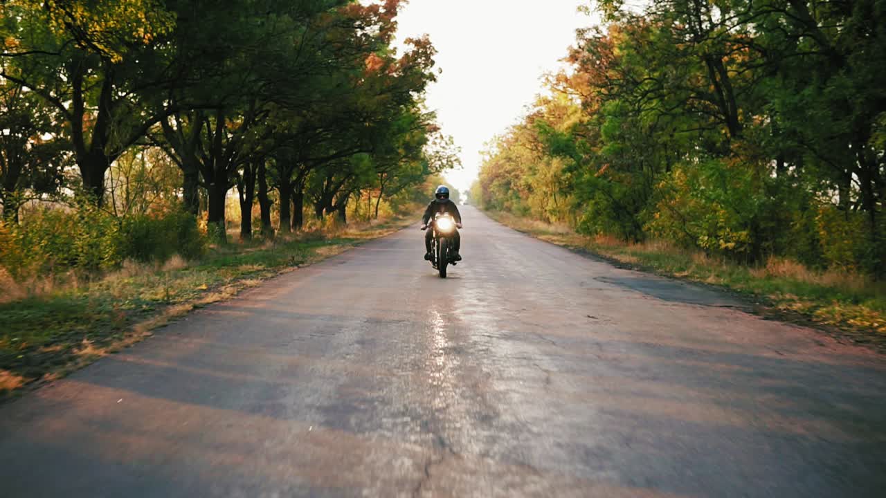 Front view of stylish man in black helmet and leather jacket riding motorcycle on and asphalt road on a sunny day in autumn