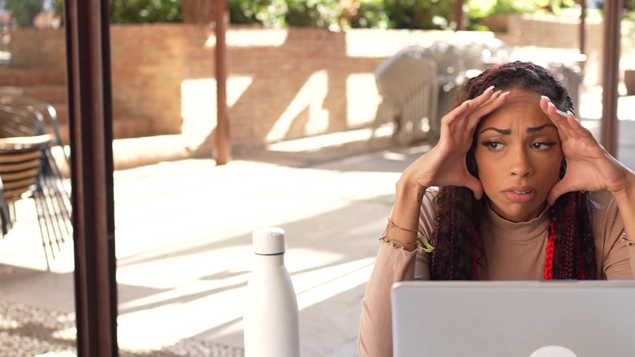 Una giovane donna gioiosa felicemente intenta con il suo laptop mentre è seduta su una graziosa terrazza di un caffè all'aperto.