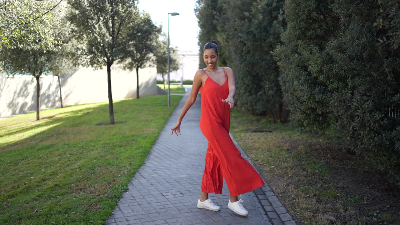 Una donna gioiosa balla nella natura mentre indossa un abito rosso brillante e colorato