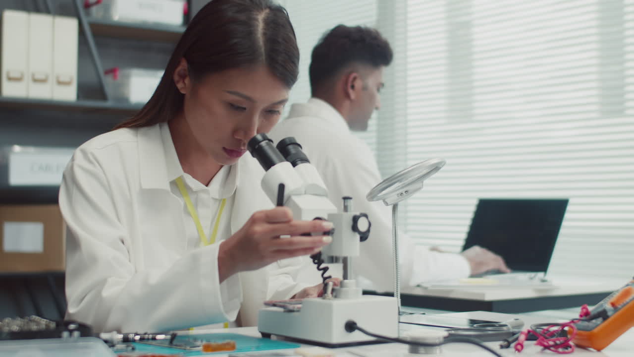 Technician Looking at Microscope when Fixing Broken Phones Component