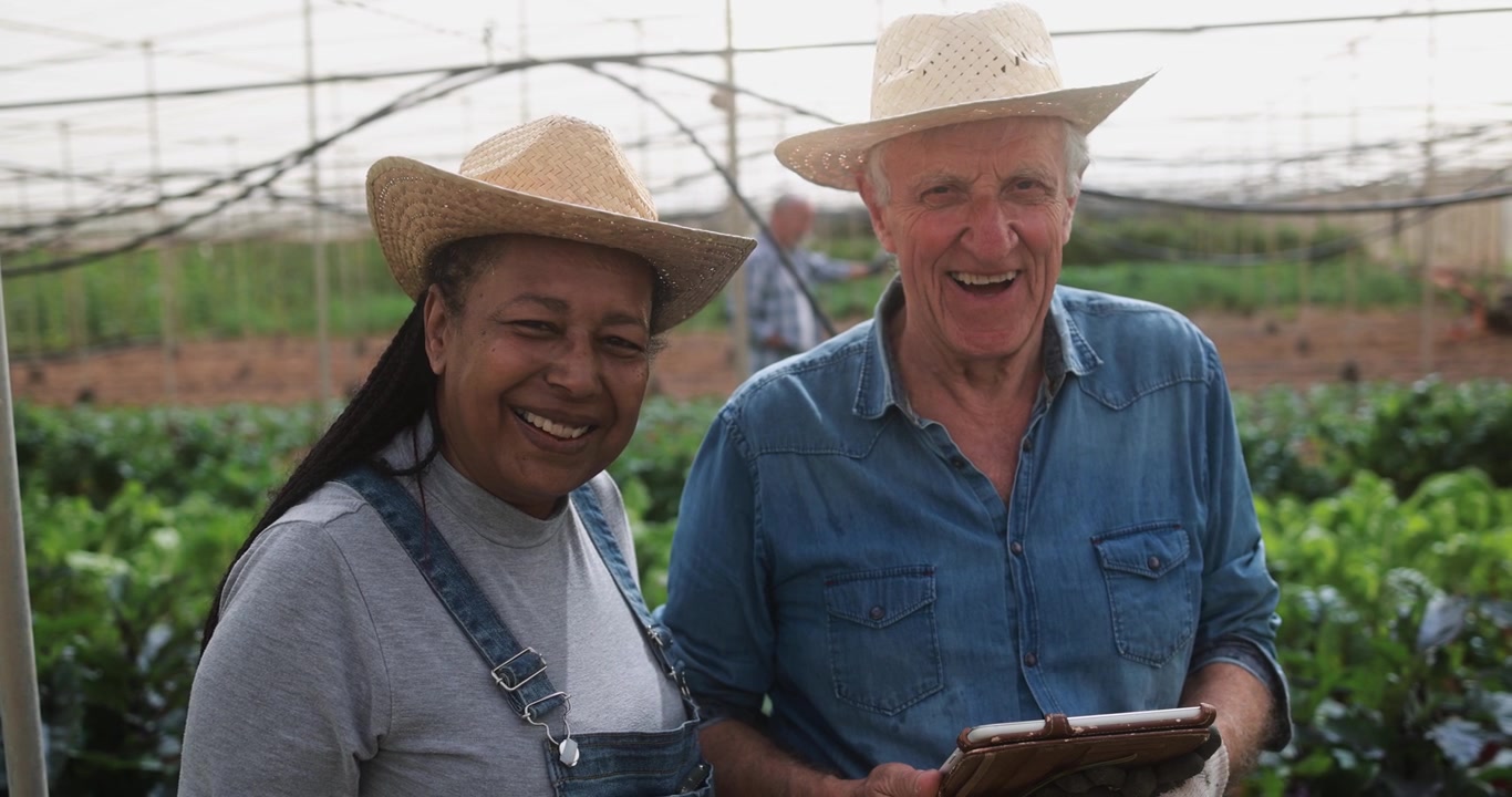 Happy Diverse Farmers Smiling in a Greenhouse with Tablet