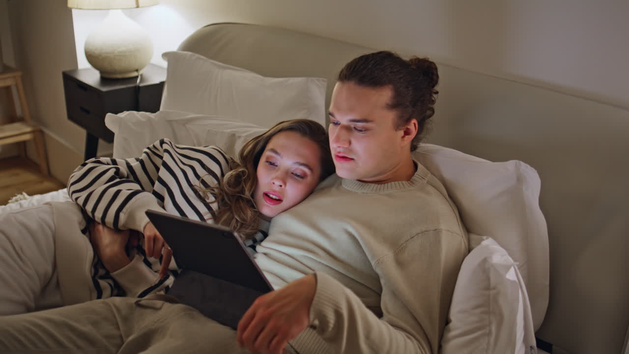 Couple watching tablet bed apartment closeup. Wife husband lying cozy bedroom