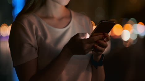 close-up of a mobile phone in the hands of a girl presses her fingers on the screen in the night city on the background of a beautiful bokeh. young businessman girl