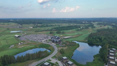 Aerial orbit of modern golf course with greens, bunkers, and water features in bright sun