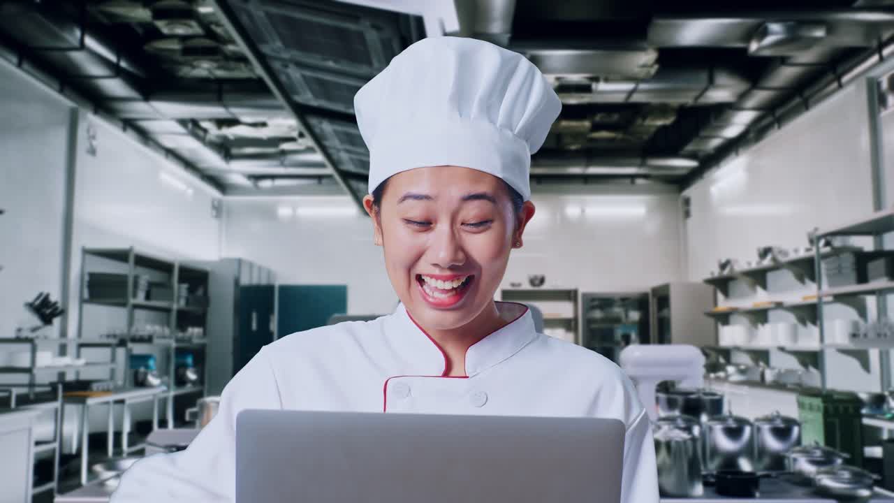 행복한 셰프가 현대적인 부에서 노트북으로 성공을 축하하고 있습니다.