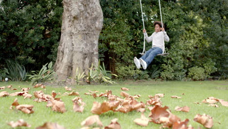 Happy african american boy swinging on tree swing in garden, in slow motion