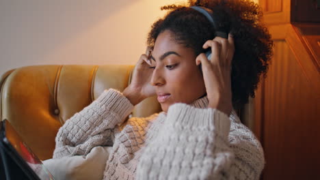 mujer rizada con auriculares cómoda en casa. mujer positiva africana viendo tableta