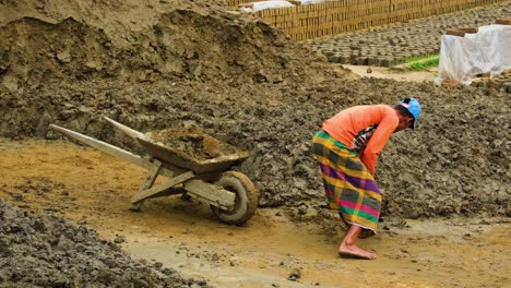 Barefoot-Bangladesh-man-shovels-soil-into-wheelbarrow-for-use-in-brick-field