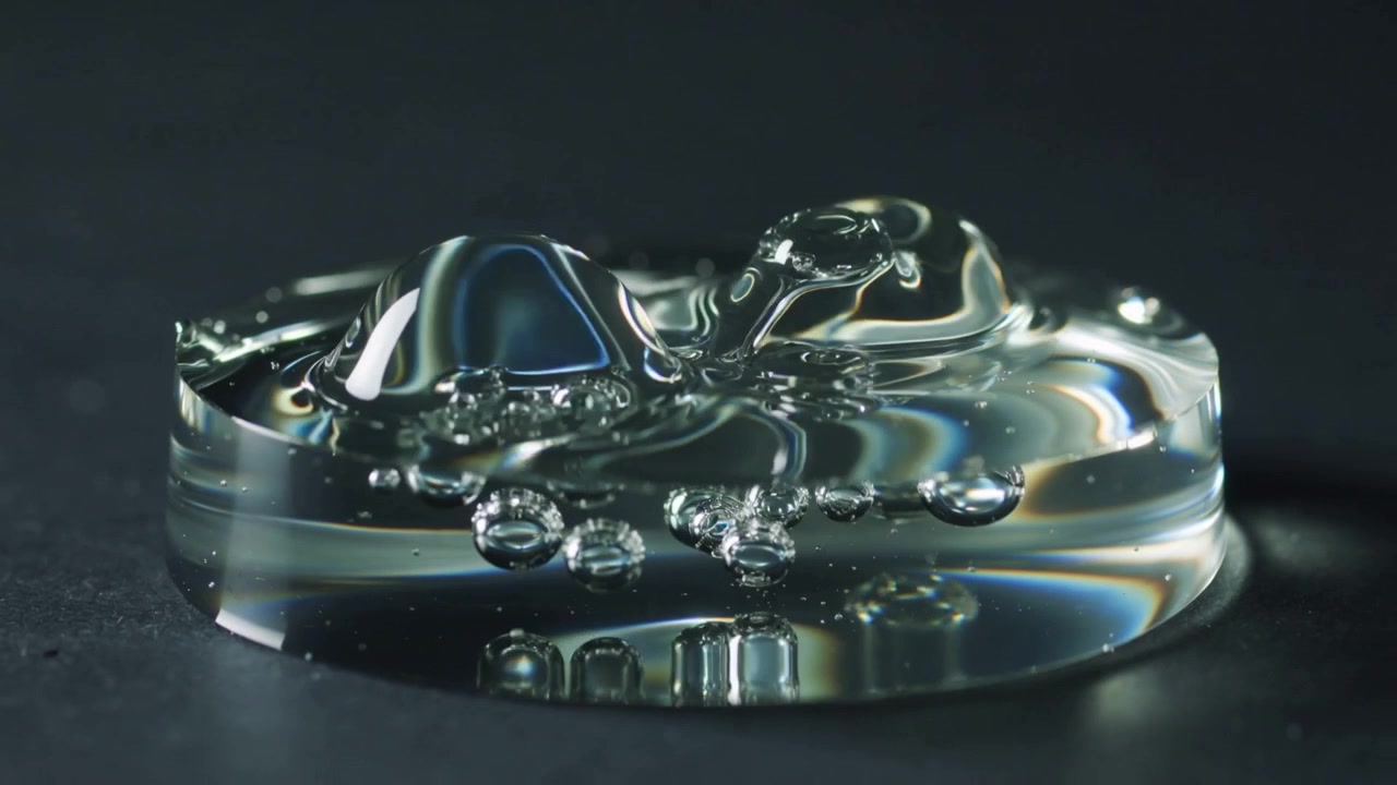 Impacting droplet creating central dome on transparent gel disc at studio tabletop, forming bubbles