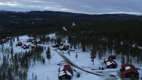 slow flight over a snowy village in a little valley framed by trees in fulufjallsbyn, sweden