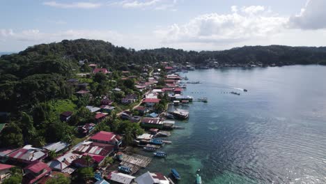 aerial - bastimentos island with coastal homes and lush green hills, panama