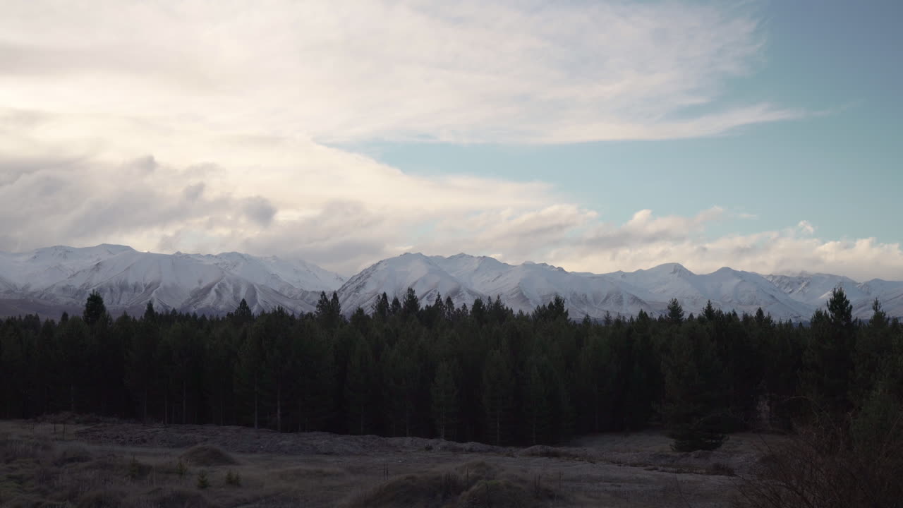 Nuvole che coprono lentamente una foresta verde e montagne innevate, inquadratura statica.