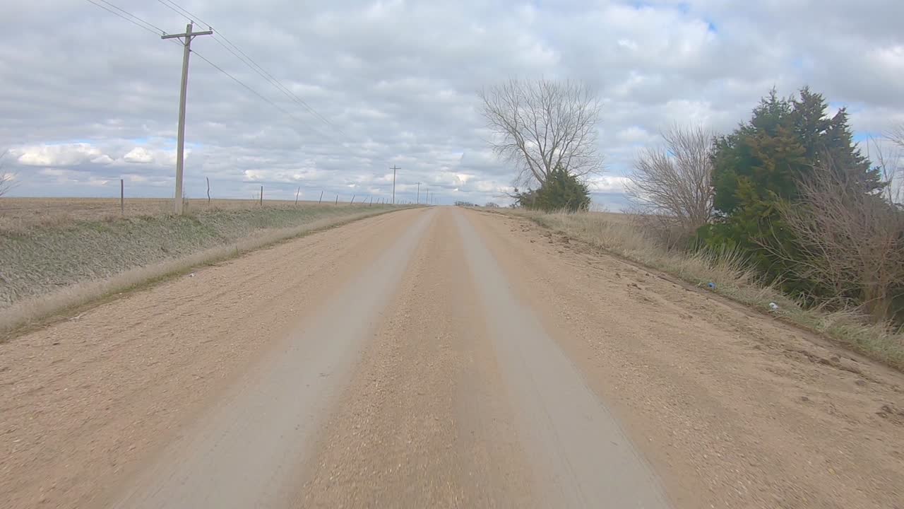 vista de la ventana trasera mientras conduce por un camino de grava entre un campo de maíz cosechado y un campo de frijoles