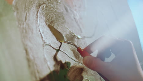 close-up of hand of artist spreading paint on canvas with palette knife