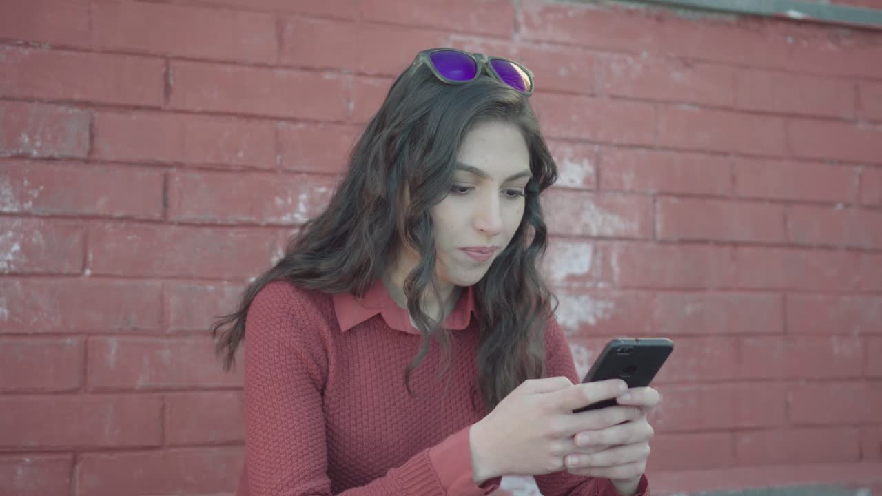 Ragazza che messaggia con uno smartphone su uno sfondo di muro di mattoni.